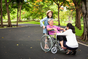 Asian senior woman in wheelchair with little child girl support,enjoy on walking,grandmother with her daughter,granddaughter having fun talk,hug,laughing together in park,elderly care,family concept