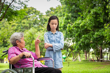 Asian senior woman in wheelchair angry,points her finger,admonishing child girl in outdoor park,grandmother emotion expression feeling,warning,reprimanding disobedient granddaughter for bad behavior
