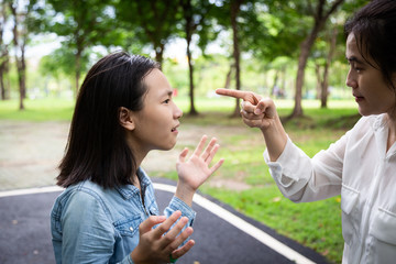 Angry adult mother quarreling,arguing with young daughter in outdoor park,parent and asian child girl shouting at each other,emotion expression feeling,relationship difficulties,family problem concept