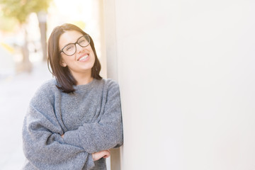 Beautiful young woman wearing glasses smiling cheerful leaning on wall, casual pretty girl at the town