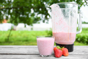 A glass of fresh cold smoothie with berries and cherrys on a wooden table, summer set, outdoor greed blured background,boke.