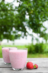 A glass of fresh cold smoothie with berries and cherrys on a wooden table, summer set, outdoor greed blured background,boke.