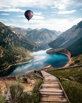 Fototapeta River in Austria alps. Vertical Wallpaper. With stairs leading down to a river and a balloon flying in the air. Partially cloudy day