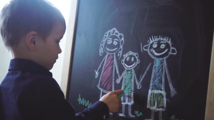 Little boy draws family on blackboard. Concept of orphanage, adoption