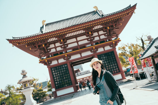 Shitennoji Temple In Osaka Japan. Red Architecture With Crowd Of People Walking Through It In Background. Woman Backpack Photographer Carrying Camera Standing Under Sunshine Blue Sky In Summer.