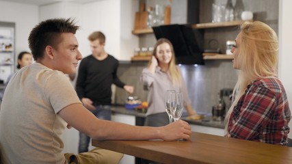 Young people with glasses of champagne talking in kitchen