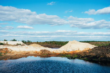 Industrial sand quarry with artificial reservoir. Sand pit. Construction industry. Sand hills agains the blue sky.