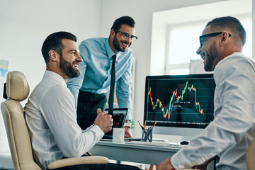 Obraz premium Successful traders. Group of young modern men in formalwear analyzing stock market data while working in the office