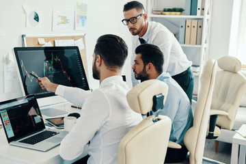 Sharing opinions. Group of young modern men in formalwear working using computers while sitting in the office