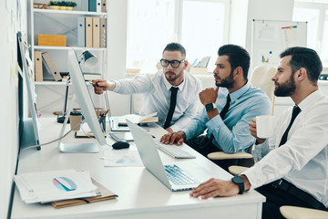 Obraz premium Successful business team. Group of young modern men in formalwear working using computers while sitting in the office