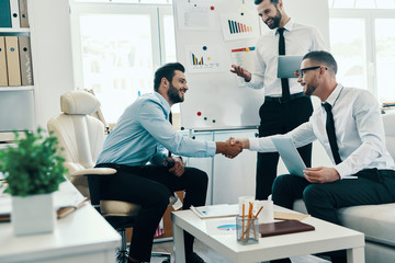 Welcome! Young modern men in formalwear shaking hands while working in the office