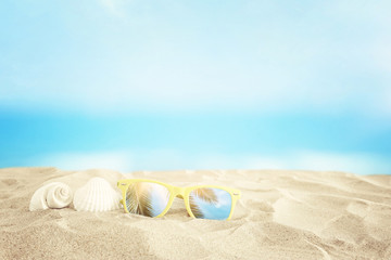 Empty sand beach, seashells and sunglasses in front of summer sea background with copy space