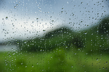  Rain drops on window glasses surface with cloudy grey and green background