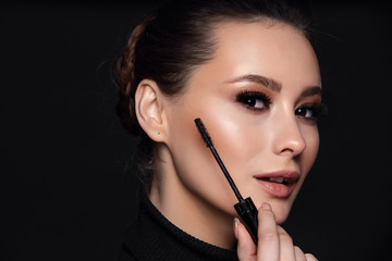 Beauty Cosmetics.Woman applying black mascara on eyelashes with makeup brush. photos of appealing brunette girl on black background.High Resolution