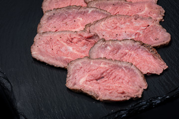 Sliced Grass Fed Juicy Corn Roast Beef on black natural stone background.