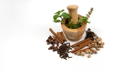 isolated dried spices such as cardamom clove cinnamon and nutmeg placed around wooden bowl with put some sweet basil, alternative drugs or nature medicine concept, selective focus