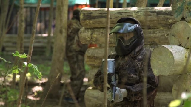Children and teenagers play paintball in the woods. One of the players Shoots from behind cover. Close up.