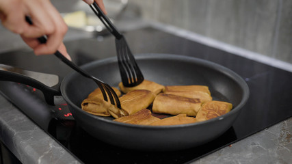 woman is roasting pancakes with fillings on a pan in her domestic electro cooker, close-up of hands