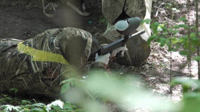 Children and teenagers play paintball. One of the players lying down shoots.