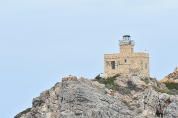 The holiday island of Ios in Greece. As the ferry sails into the sheltered bay a lighthouse stands sentinel above jagged rocks at the ports entrance.