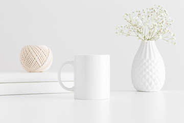 Mug mockup with workspace accessories and a gypsophila on a white table.