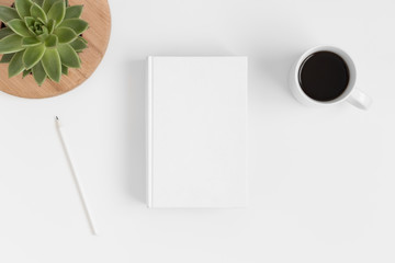 Top view of a white book mockup with workspace accessories and a succulent plant on a white table.
