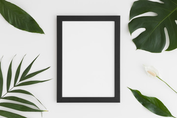 Top view of a black frame mockup with tropical leaves decoration. Portrait orientation.