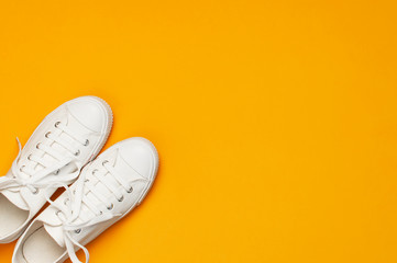 White female fashion sneakers on yellow orange background. Flat lay top view copy space. Women's shoes. Stylish white sneakers. Fashion blog or magazine concept. Minimalistic shoe background, sport