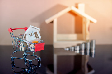 Buying property or real estate investment concept. Home mortgage and lease. Bank loan interest rate. Wooden house models in mini shopping cart with step of coins stacked on glossy table.