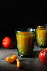Still life of fresh delicious sweet nectarines with droplets of water and juice in turquoise vintage glasses on dark background. Low key.