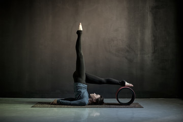 Woman practicing yoga, doing Salamba Sarvangasana exercise, supported Shoulder stand pose using wheel props. Studio shot