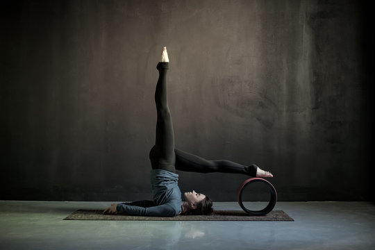 Woman practicing yoga, doing Salamba Sarvangasana exercise, supported Shoulder stand pose using wheel props. Studio shot