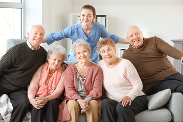 Young caregiver with group of senior people in nursing home