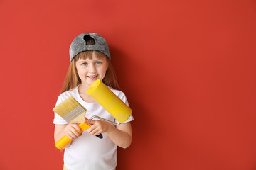 Cute little girl with paint roller and brush on color background