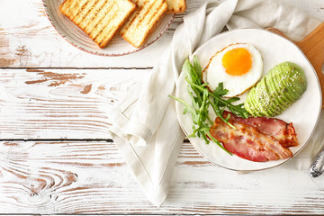 Plate with tasty fried egg, avocado and bacon on wooden table