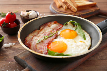 Frying pan with tasty eggs and bacon on wooden table