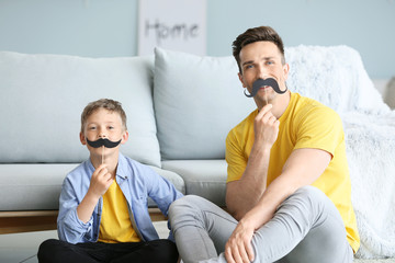 Portrait of funny father and son with fake mustache at home