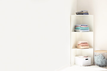 Rack with stacks of clean clothes near white wall