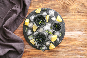 Slate plate with black caviar, ice cubes and lemon on wooden background
