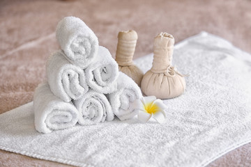 Fototapeta na wymiar Rolled towels, herbal bags and flower on table in spa salon