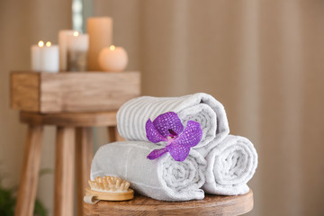 Fototapeta na wymiar Rolled towels, flower and massage brush on table in spa salon