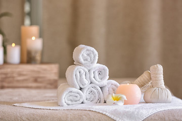 Fototapeta na wymiar Rolled towels, herbal bags, candle and flower on table in spa salon