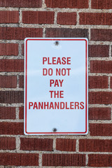 Sign that says please do not pay the panhandlers posted on brick wall - close-up