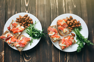 Wholemeal bread with salmon on white plate. Arugula and almond with lemon. Healthy sandwiches. Omega-3 for snack. Proper nutrition. Sport food.