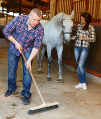 Male worker cleaning floor at stabling, woman farmer standing