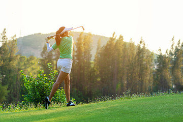 Healthy Sport. Asian Sporty woman golfer player doing golf swing tee off on the green evening time,...