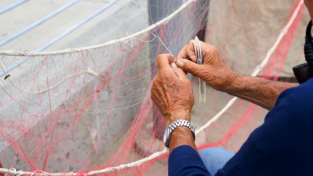 Old fisherman reparing fishing net.