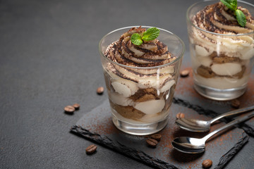 Classic tiramisu dessert in a glass on stone serving board on dark concrete background