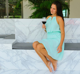 a young, beautiful girl, in a mint-colored dress, holds a glass of red wine, looks into the distance. soft focus