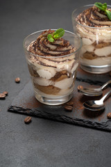 Classic tiramisu dessert in a glass on stone serving board on dark concrete background